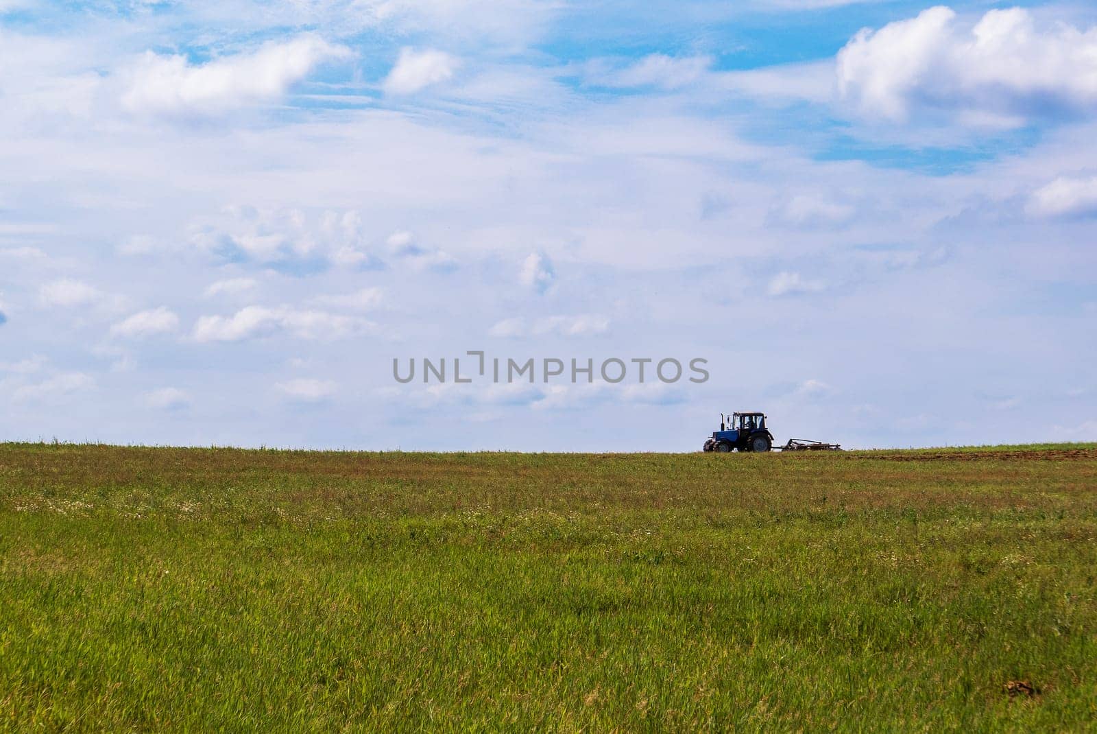 Tractor working in the field, plowing the land, preparing for sowing. View of the field and tractor in the distance against a blue sky with clouds