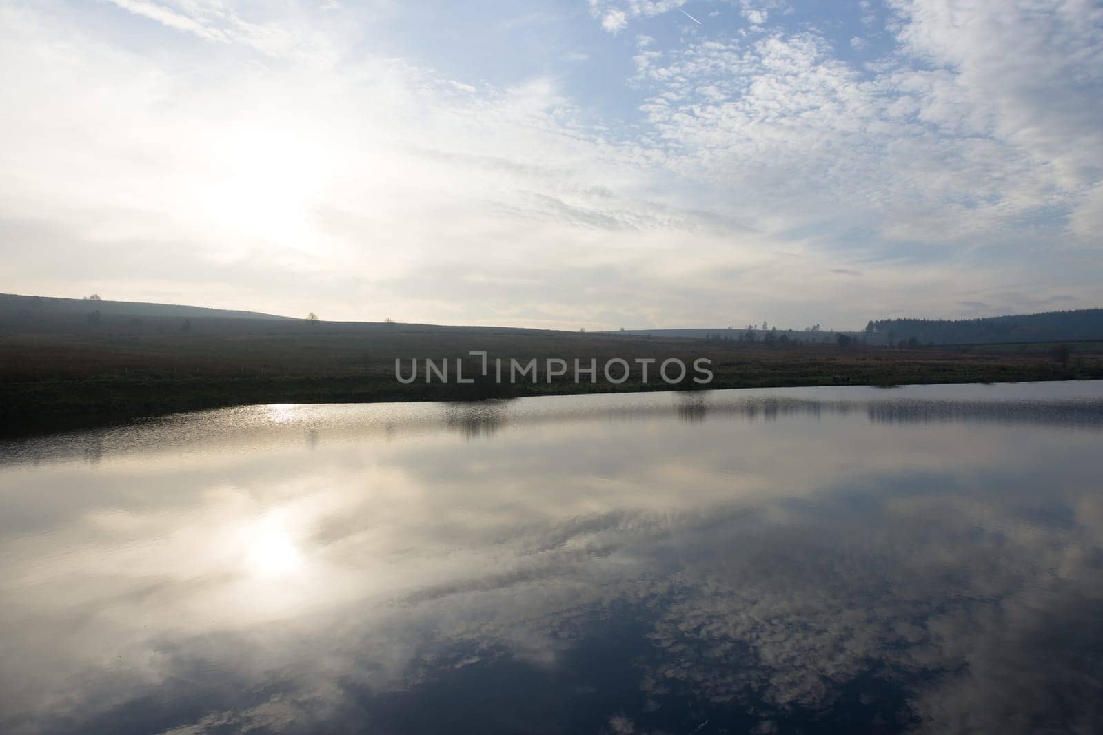 Horizontal wide angle image of a bright winters sky reflected in a calm reservoir. Redmires upper reservoir shown here very still and flat calm.