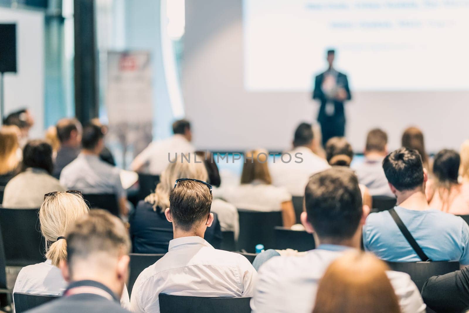 Speaker giving a talk in conference hall at business event. Rear view of unrecognizable people in audience at the conference hall. Business and entrepreneurship concept.