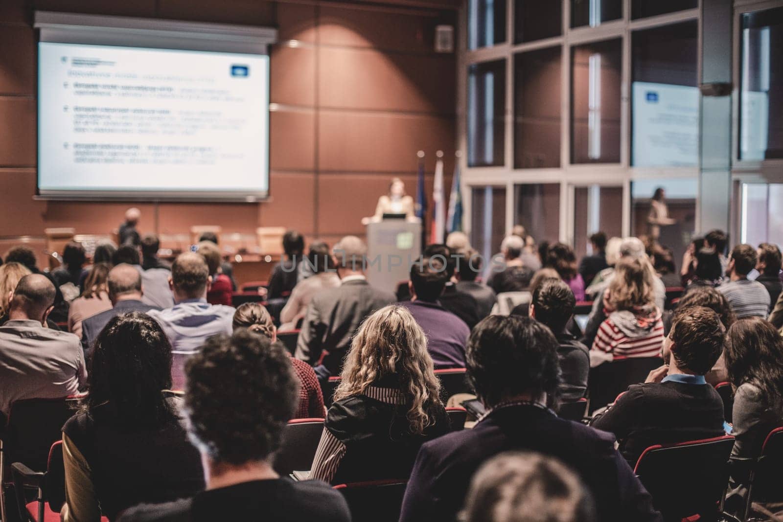 Business and entrepreneurship symposium. Speaker giving a talk at business meeting. Audience in the conference hall. Rear view of unrecognized participant in audience.