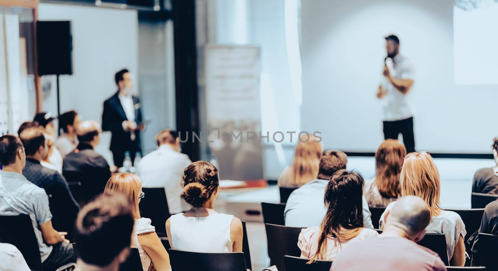 Speaker giving a talk in conference hall at business event. Rear view of unrecognizable people in audience at the conference hall. Business and entrepreneurship concept.