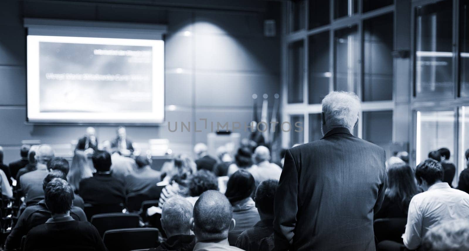 I have a question. Group of business people sitting at the chairs in conference hall. Businessman raising his arm. Conference and Presentation. Business and Entrepreneurship.