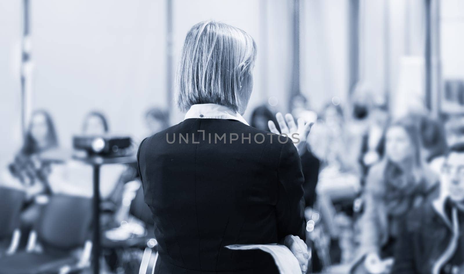 Female speaker giving a talk on corporate business conference. Unrecognizable people in audience at conference hall. Business and Entrepreneurship event.