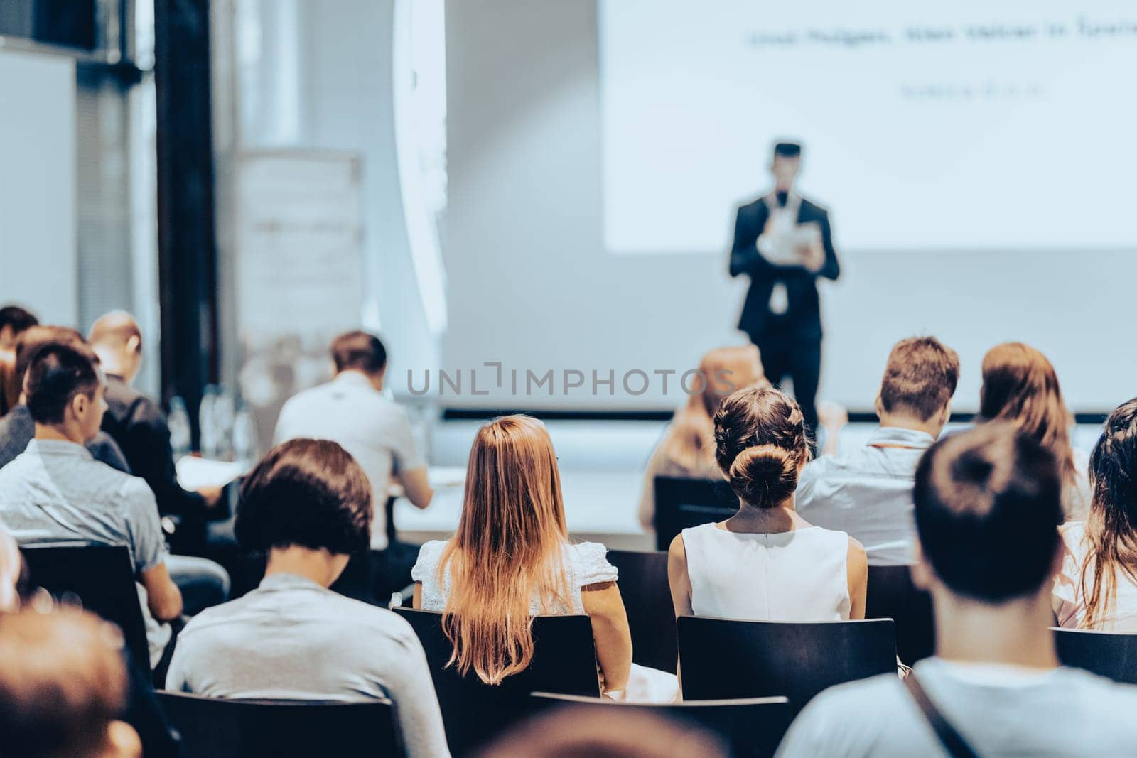 Speaker giving a talk in conference hall at business event. Rear view of unrecognizable people in audience at the conference hall. Business and entrepreneurship concept.