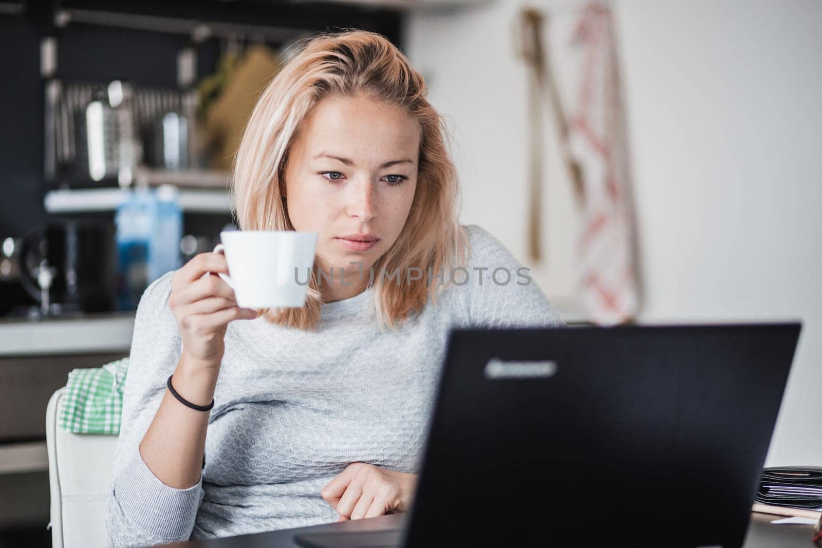 Female freelancer in her casual home clothing working remotly from her dining table in the morning. Home kitchen in the background