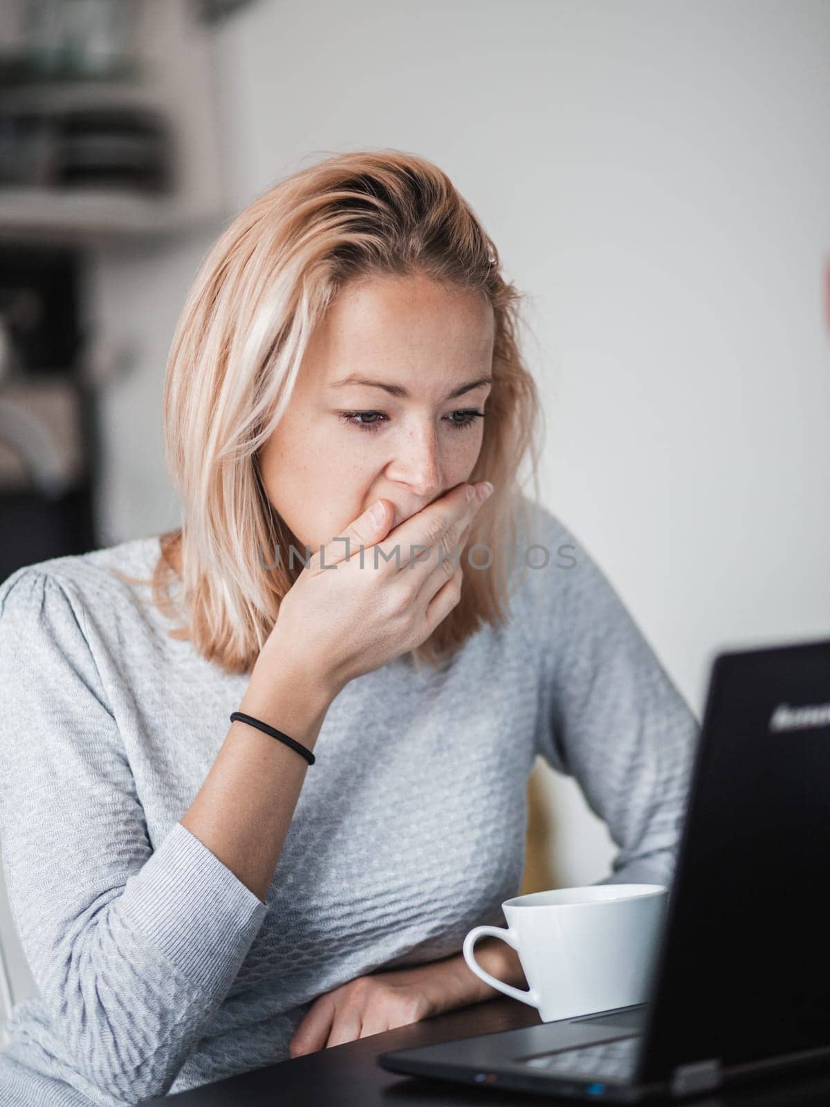Female freelancer in her casual home clothing working remotly from her dining table in the morning. Home kitchen in the background
