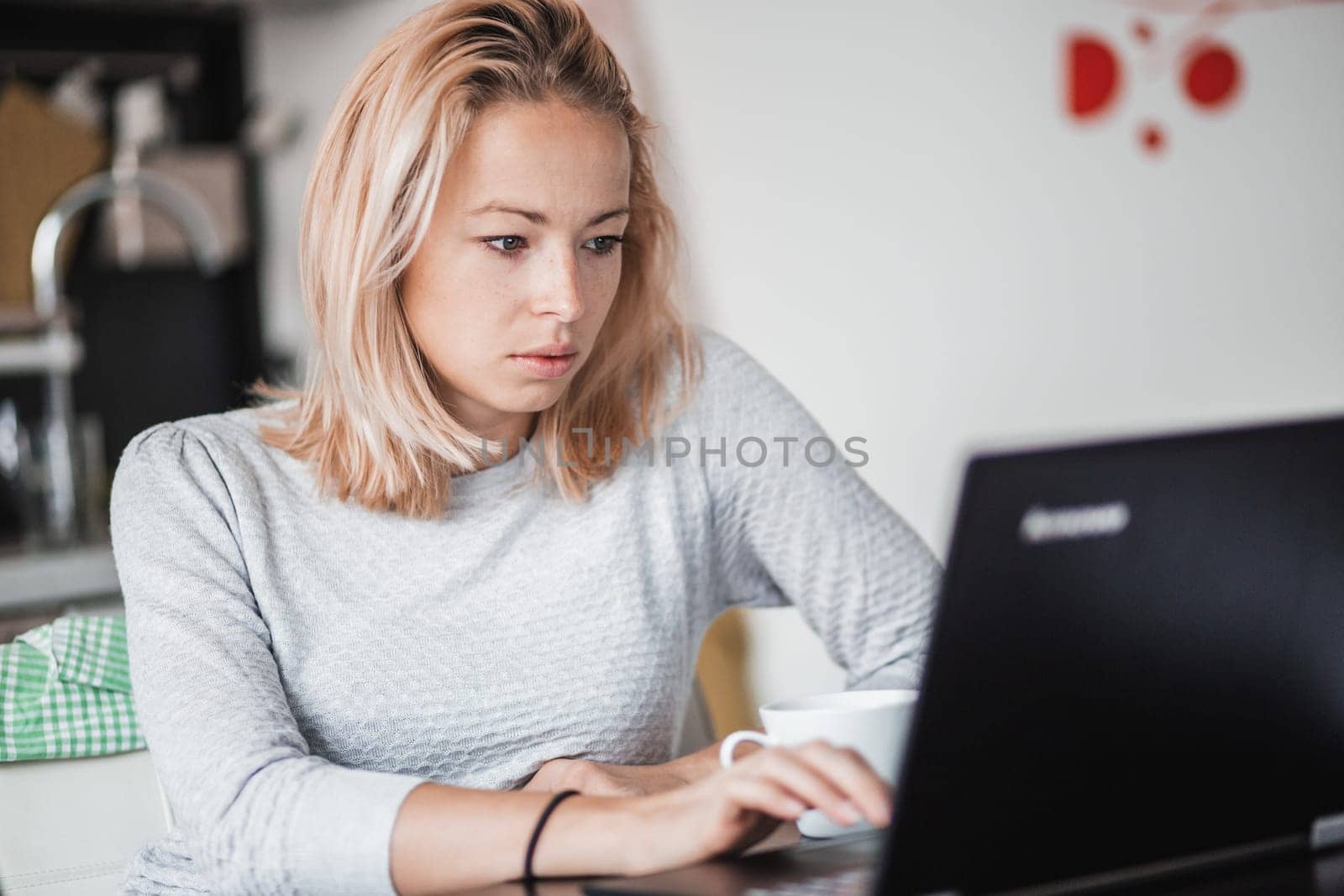 Female freelancer in her casual home clothing working remotly from her dining table in the morning. Home kitchen in the background
