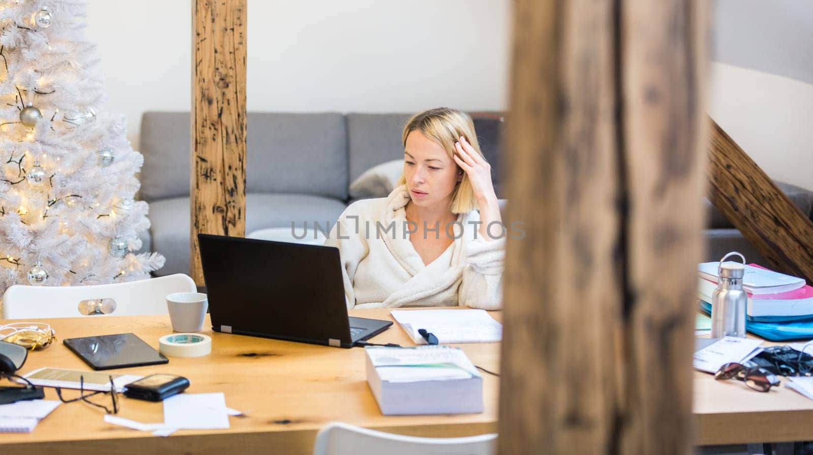 Young businesswoman wearing cosy warm bathrobe working remotly from home in winter Christmas time during 2020 corona virus pandemic. Work from home, selter in place, concept.