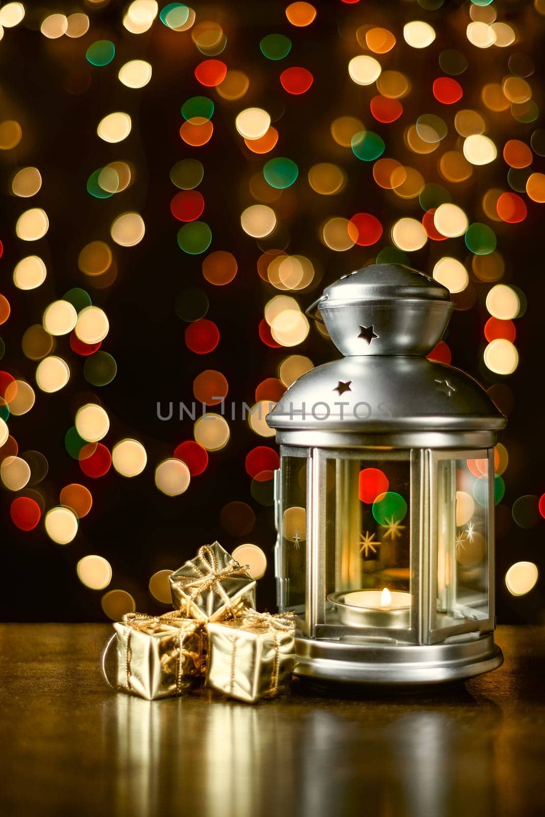 Christmas composition: a lantern with candles, bright shiny boxes with gifts, blurred bokeh lights in the background.