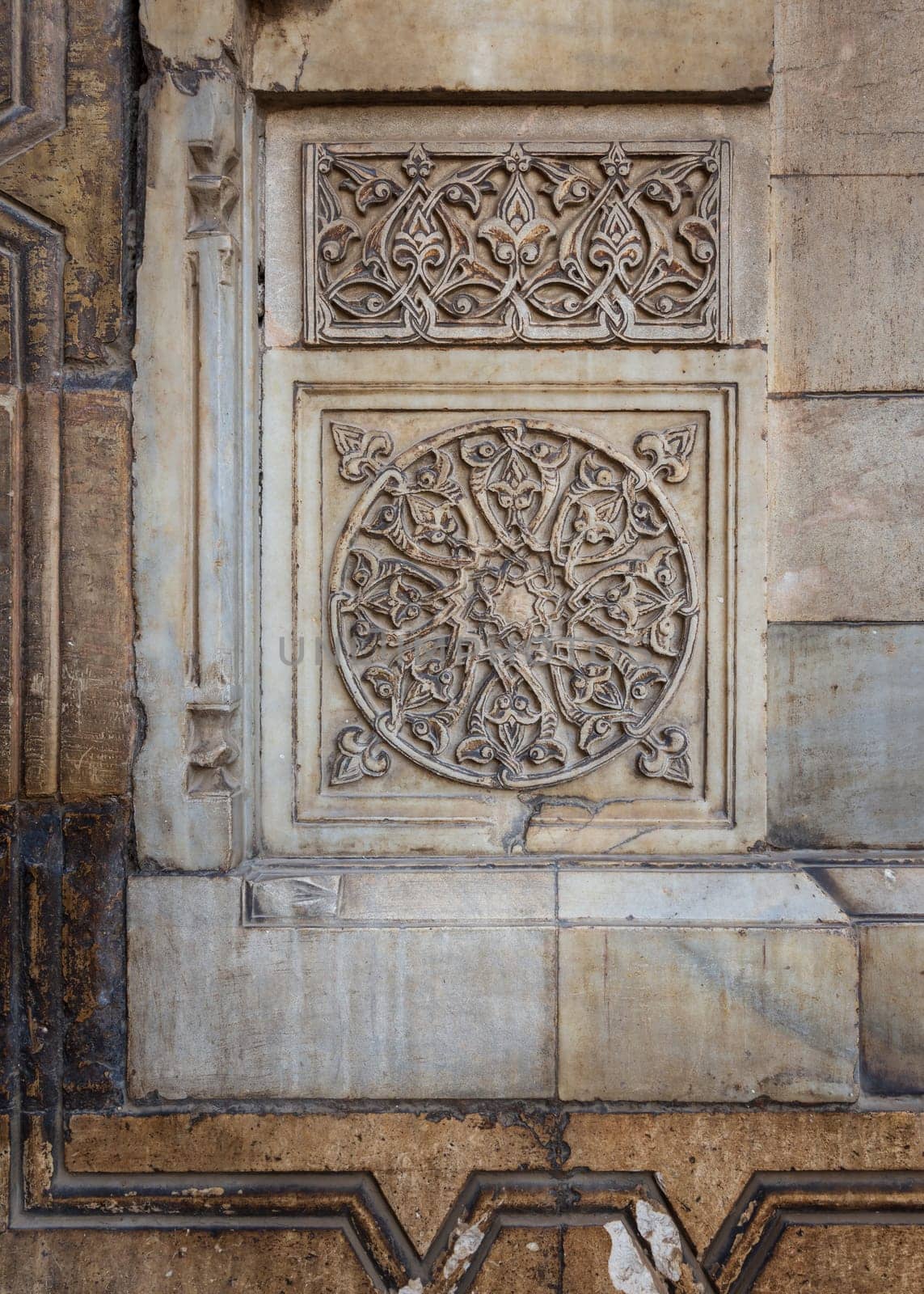 Round floral patterns framed by geometrical patterns carved into the exterior ancient stone wall of Sultan Hasan Mosque, Old Cairo, Egypt