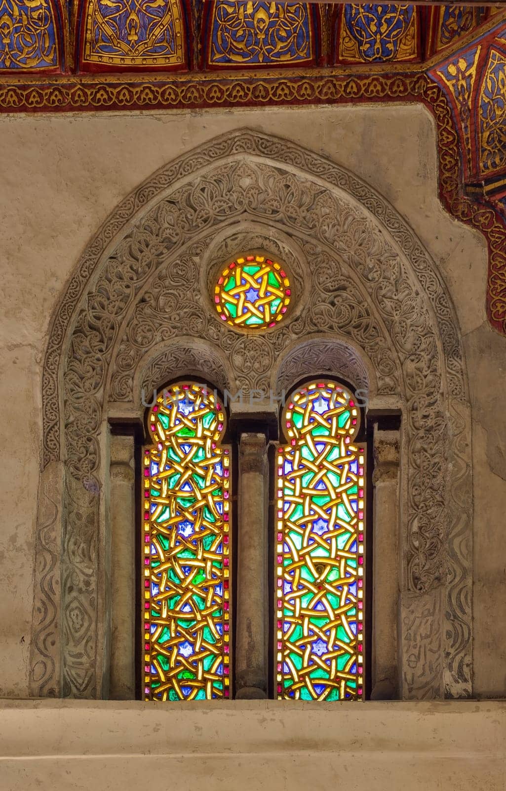 Two adjacent perforated stucco arched windows decorated with colorful stain glass with geometrical and floral patterns, at Mamluk era public historical Qalawun complex, Moez Street, Cairo, Egypt