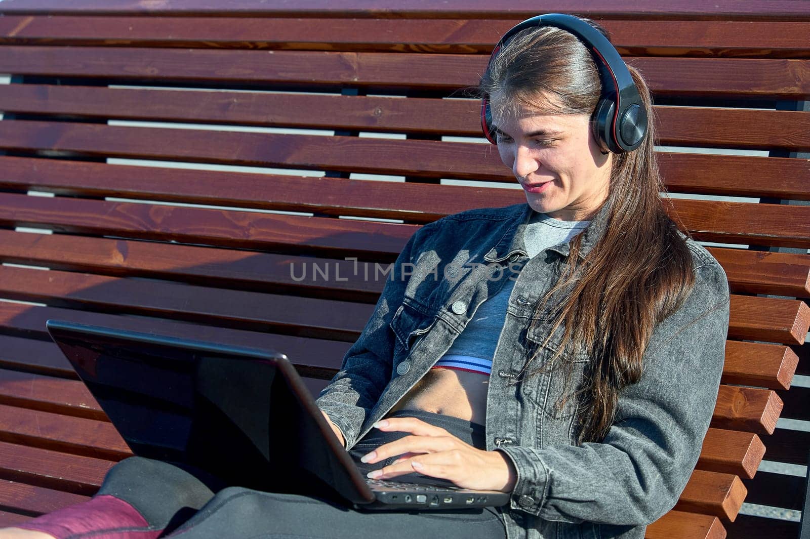 A woman with a laptop sits on an outdoor bench and works online. High quality photo
