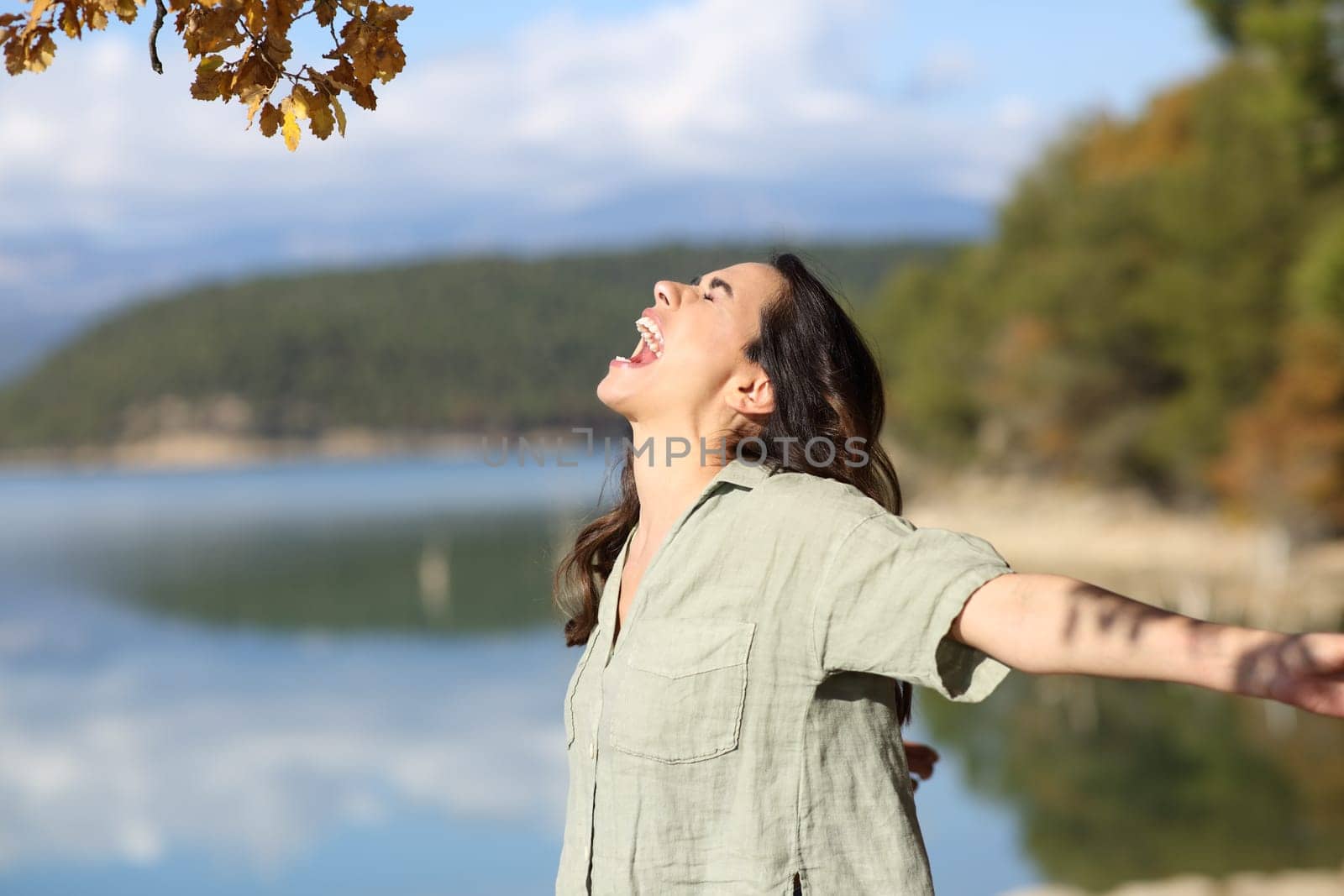 Side view portrait of a happy woman outstretching arms in a mountain lake