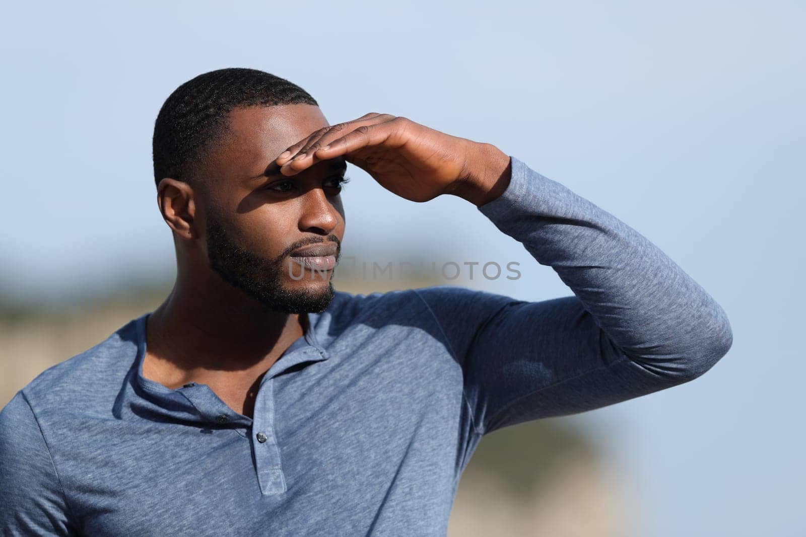 Serious man with black skin searching protecting from sun with a hand in the mountain a sunny day