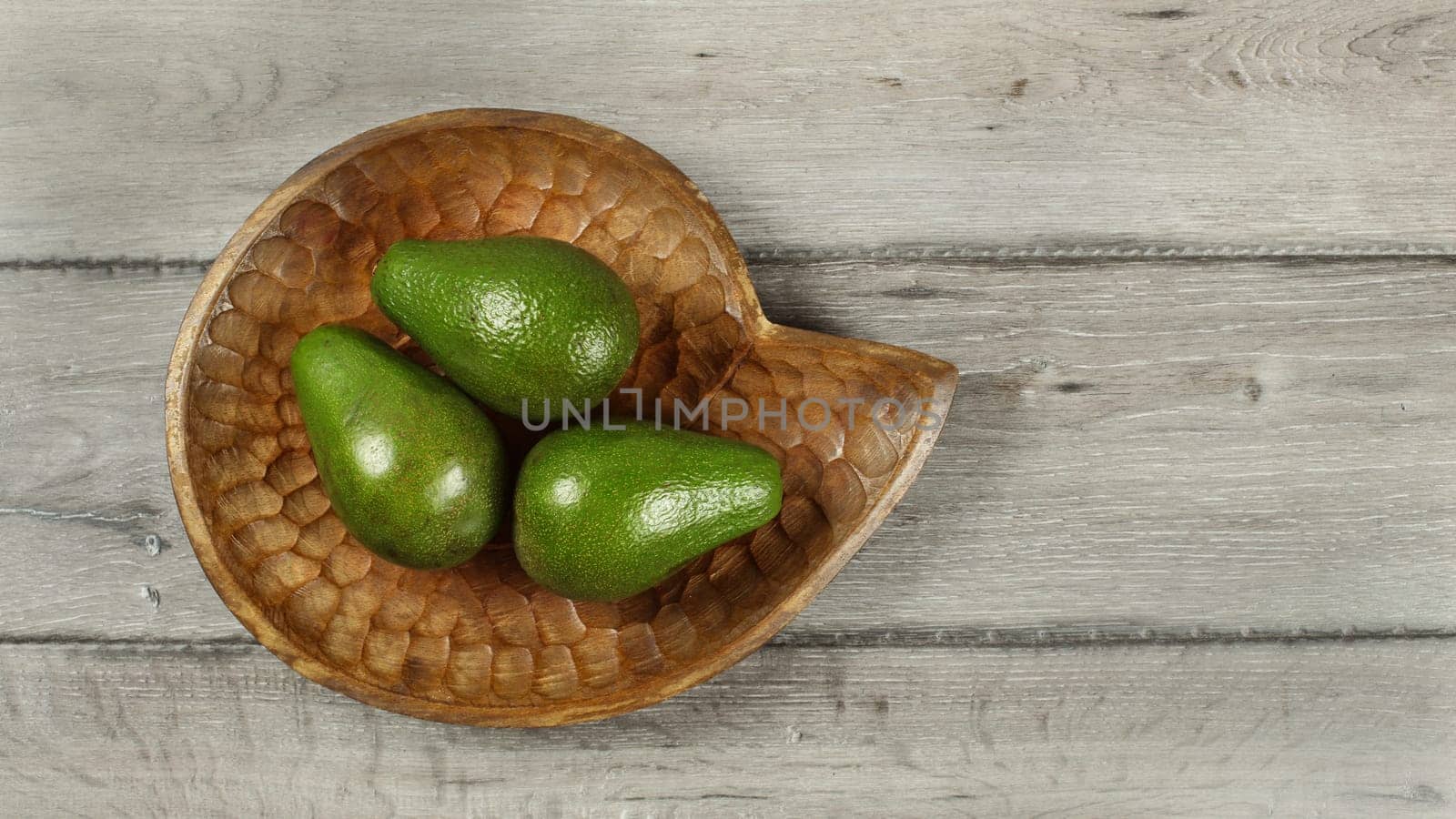 Tabletop view, three avocado pears on wooden carved bowl