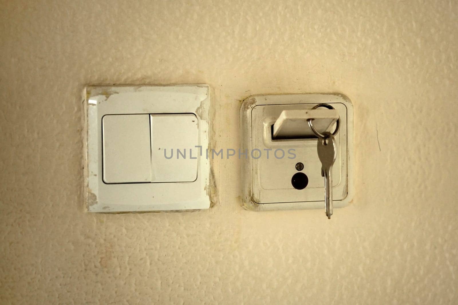 Classic mechanic key with card in slot to activate electricity in hotel room. Old dirty wall and socket.