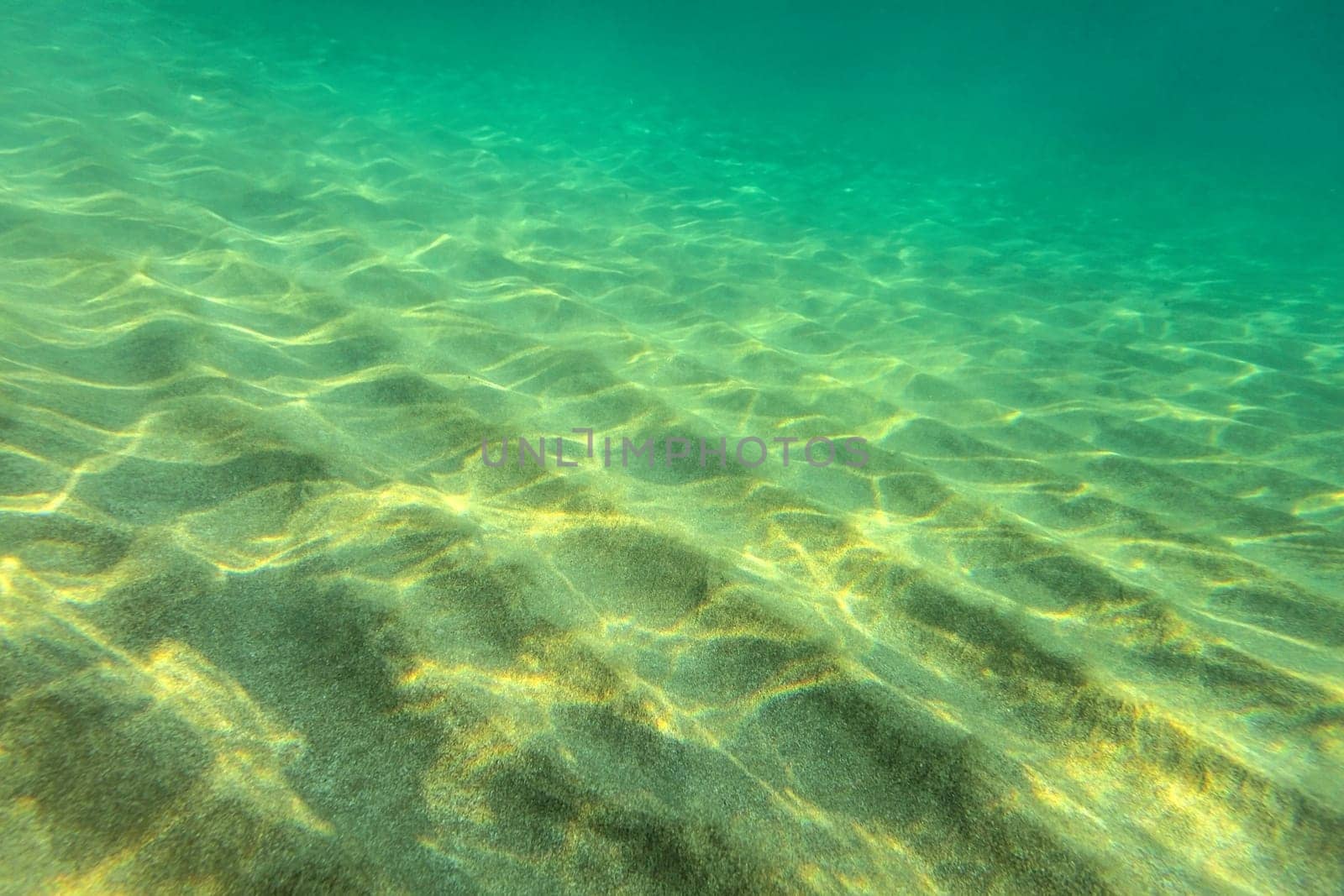 Sandy sea bottom, small sand "dunes"" lit by sun, underwater photo, abstract marine background."