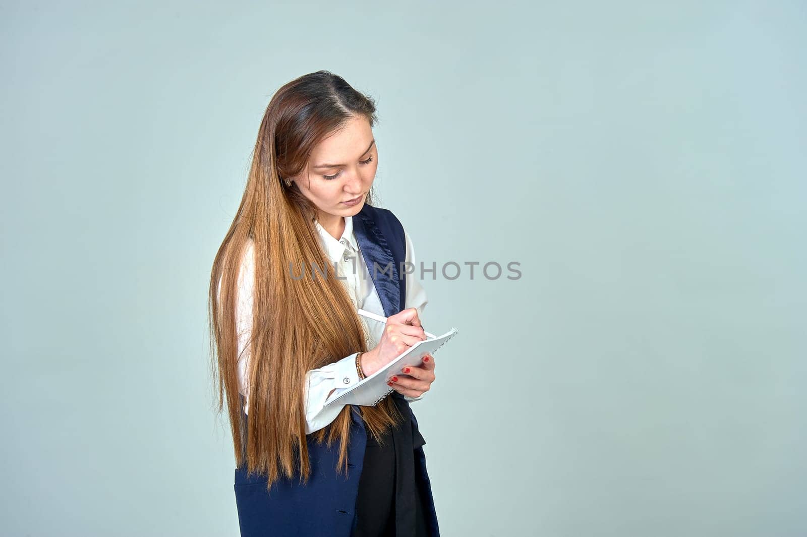A young woman writes with a pen in a notebook on a white background. High quality photo