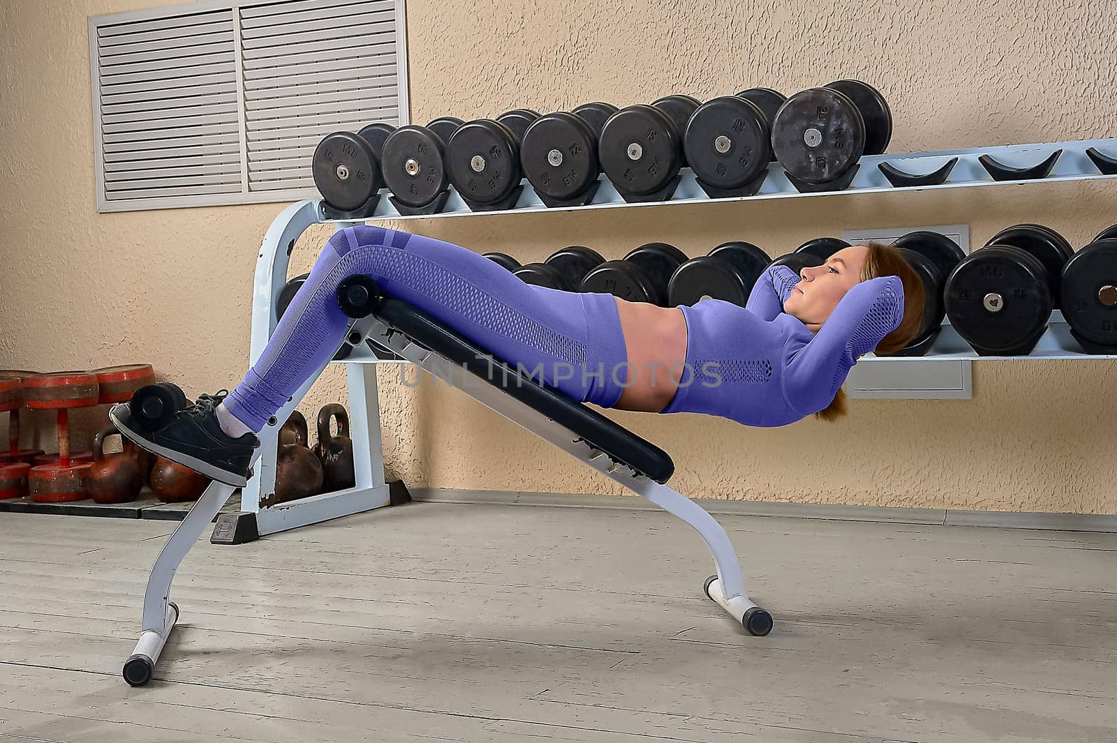 A beautiful young woman shakes her abs on a bench in the gym. High quality photo
