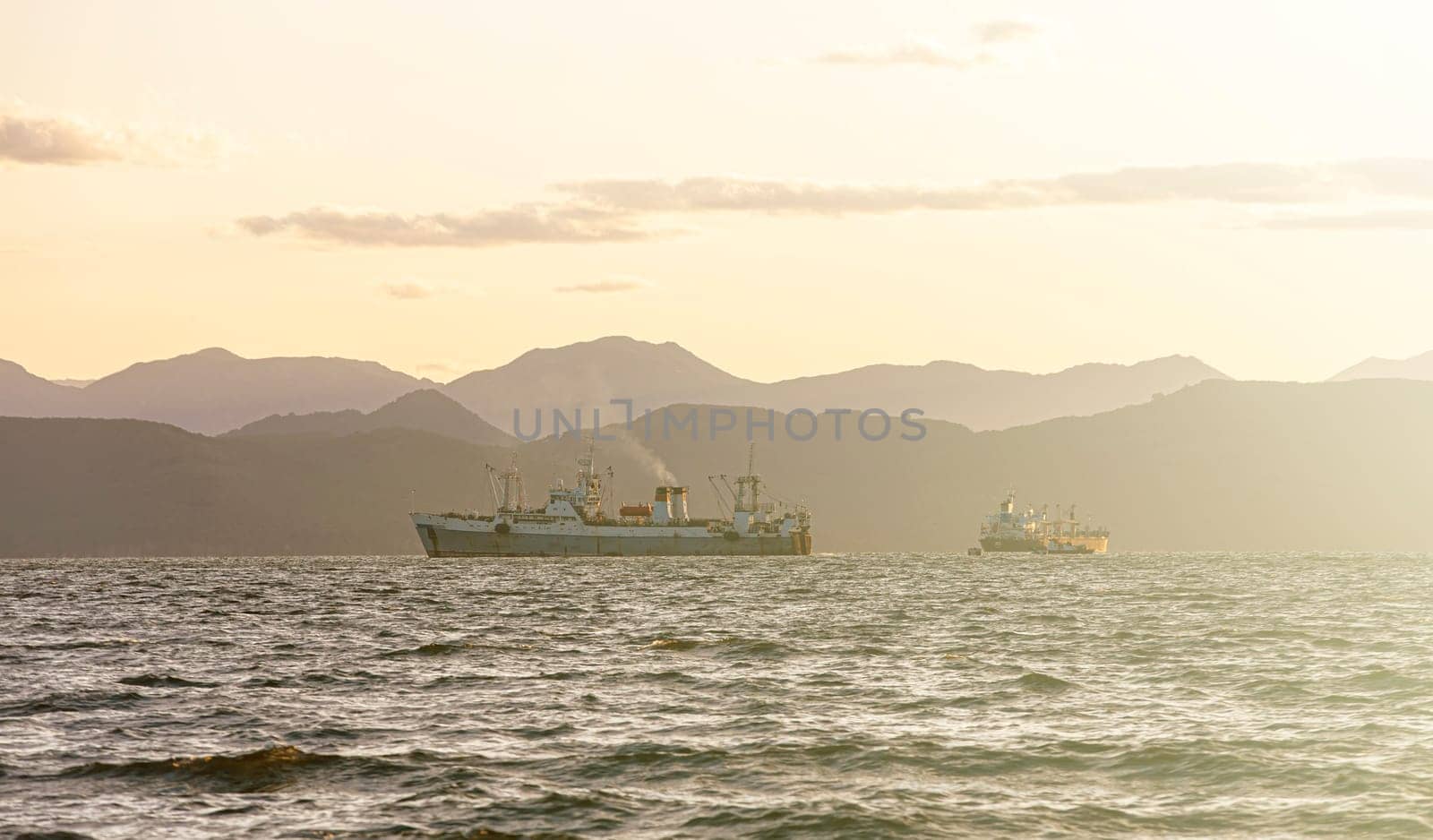 The fishing ship in the sea at sunrise on the background of mountains