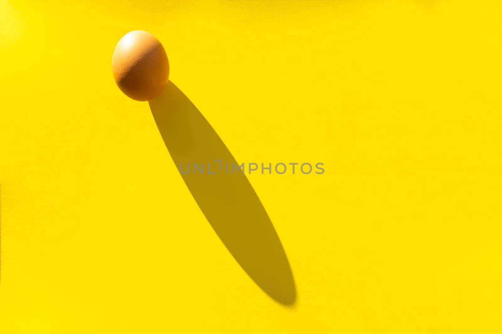 Brown organic raw egg on a yellow background with a hard shadow.