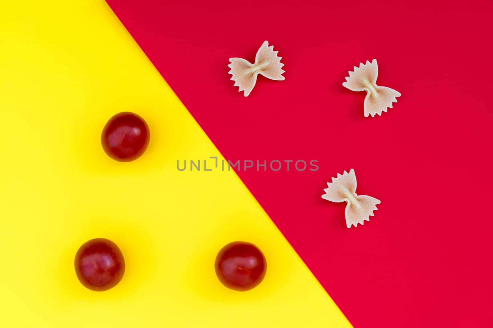 Three pieces of farfalle paste and three cherry tomatoes on a contrasting background