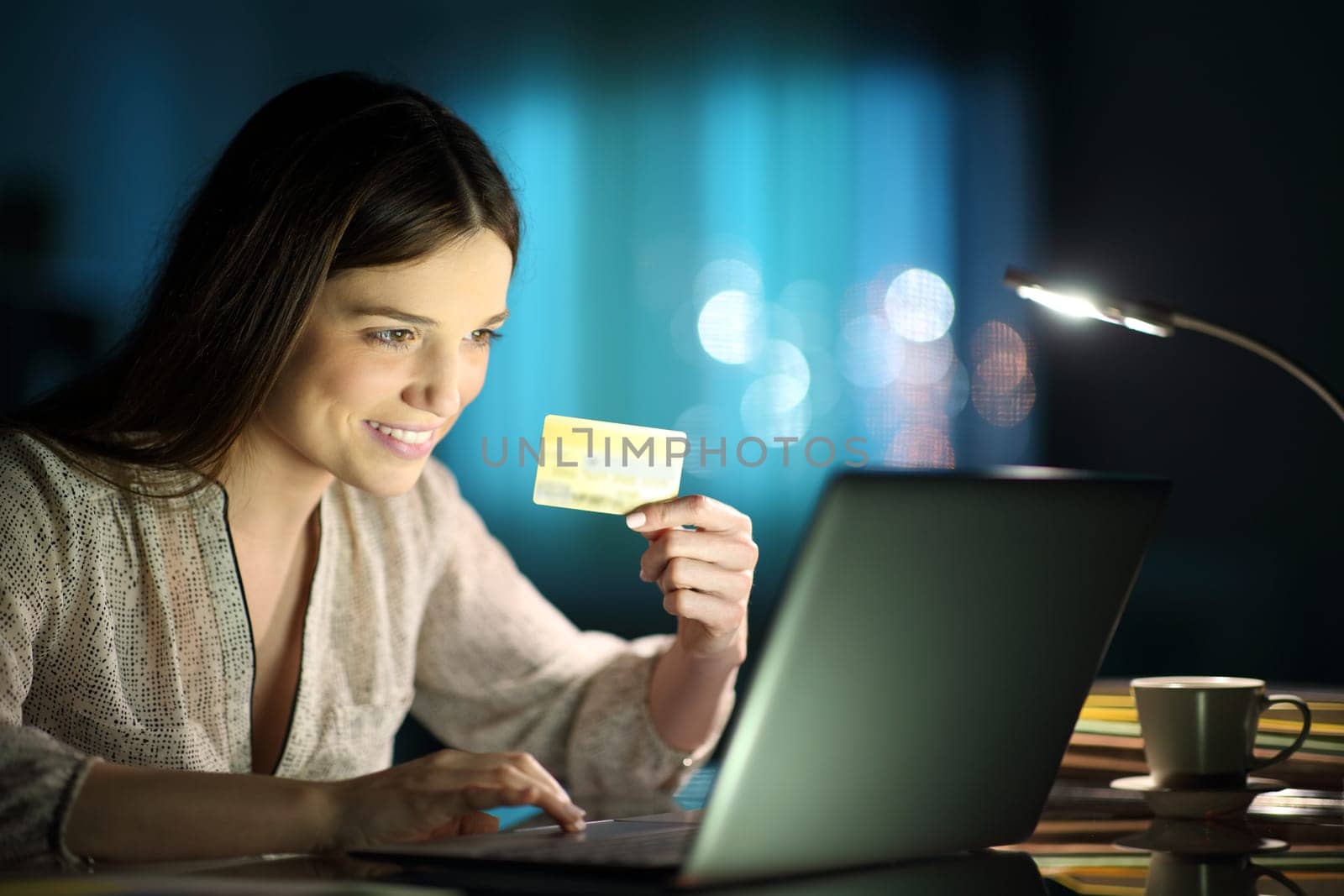 Happy woman holding credit card buying on line with a laptop in the night at home