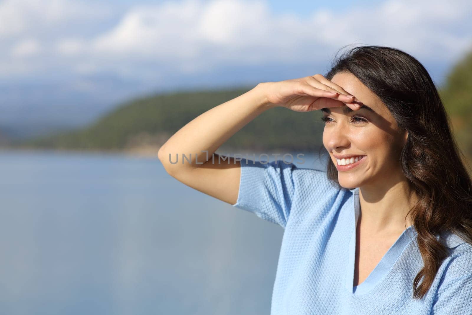 Happy woman looking away protecting from sun with hand in a lake