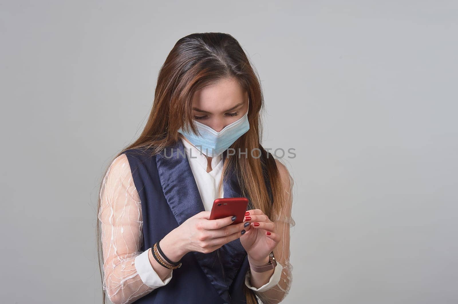 A girl in a medical mask with a phone in her hands. High quality photo