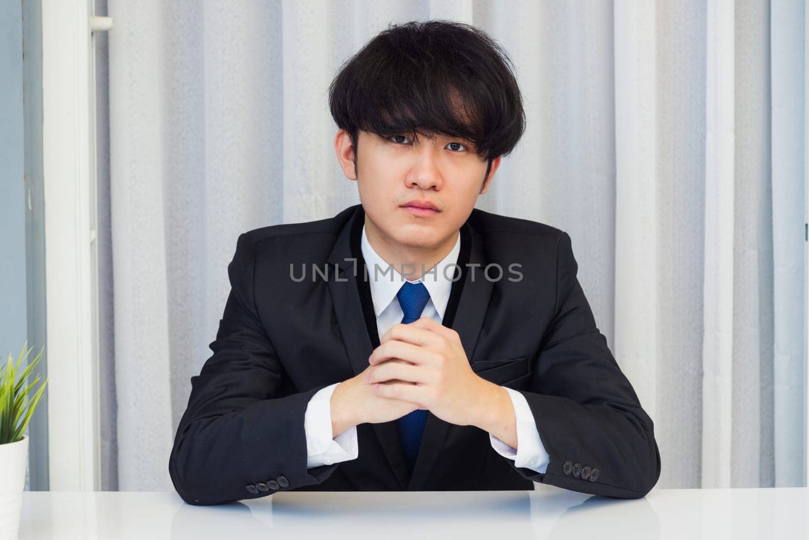 Work from home, Close up face of Asian young businessman video conference call or facetime he looking to camera sitting and holding hands to listen to colleagues explain the work on desk at office