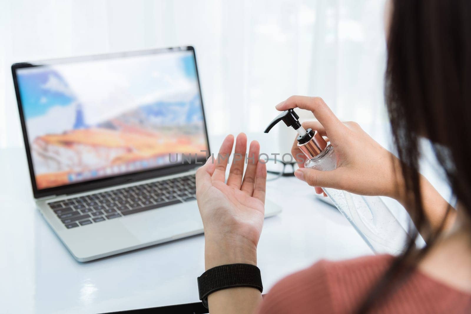 Work from home, Back of Asian young business woman video conference meeting online on front laptop computer cleaning hands with sanitizer alcohol gel pump quarantines disease coronavirus or COVID-19