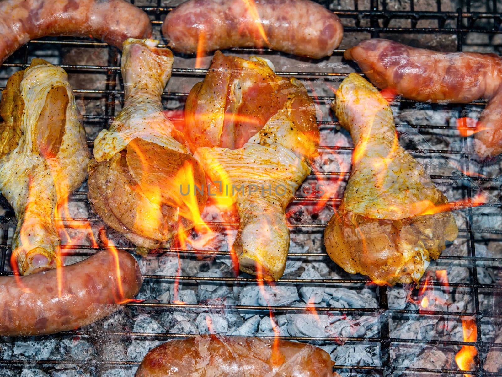 Chicken legs and meat sausages on an iron barbecue net over the fire. Cooking over a fire. Grill mesh. Chicken and meat sausages. Healthy eating. Food in nature. Menu of dishes. Background image.