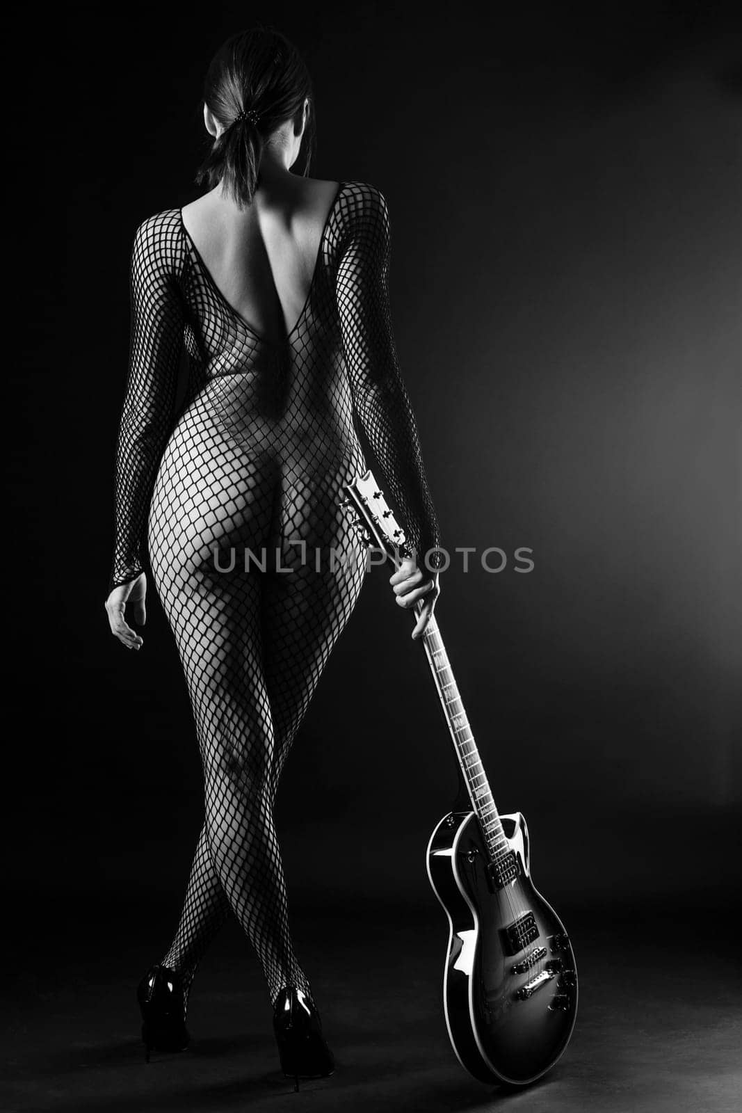 Sexy woman from behind in fishnet body stocking, standing and holding a electric guitar.