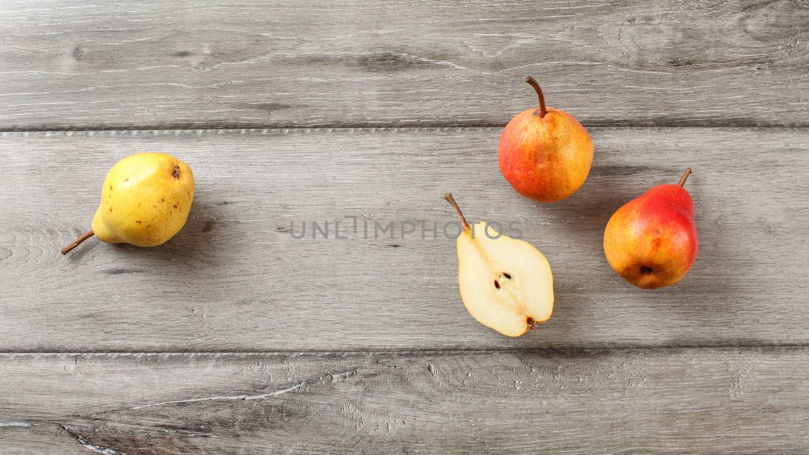 Table top view, ripe pears, one cut in half, on gray wood desk.