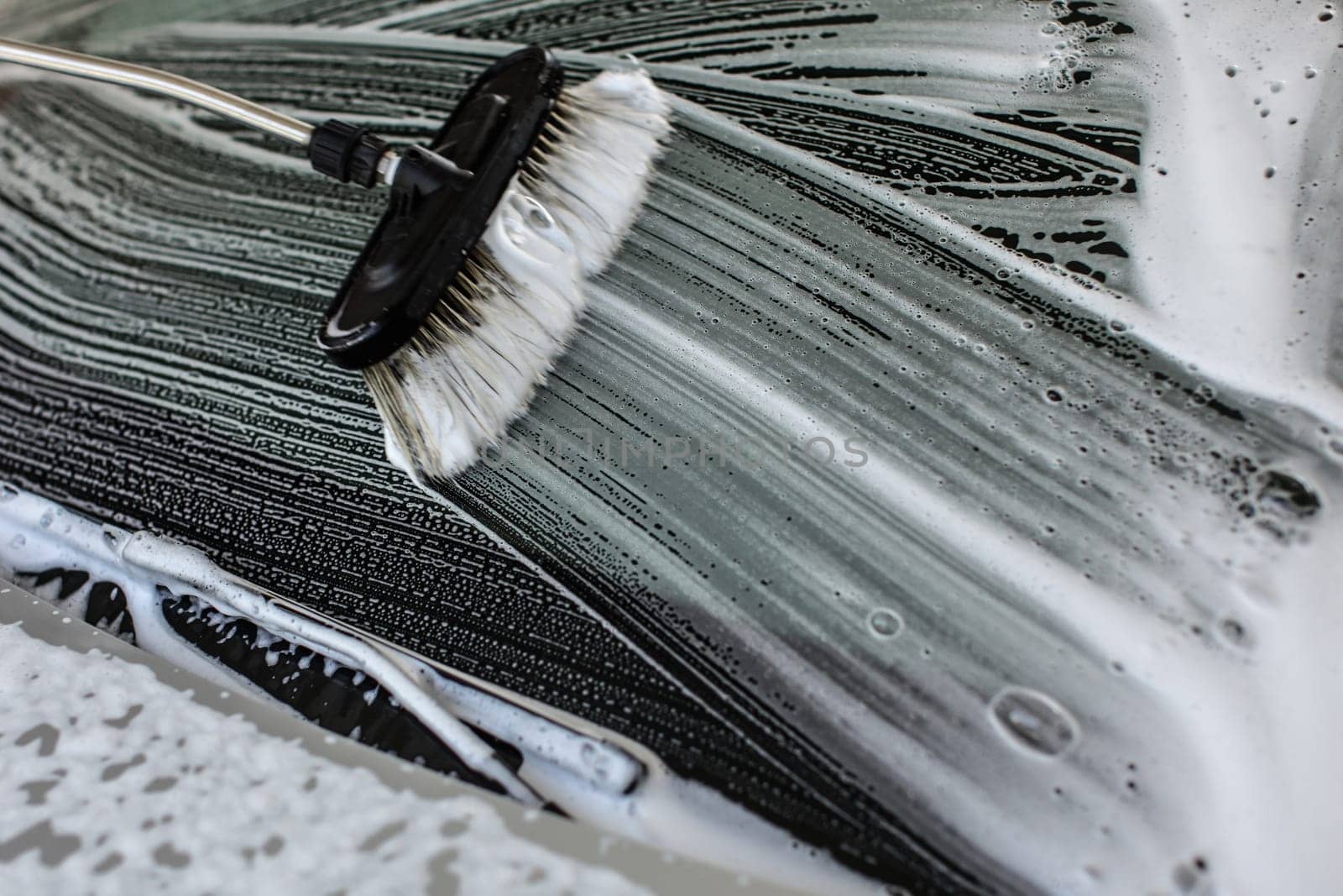 Brush leaving strokes in white shampoo and foam on a window of car washed in carwash.