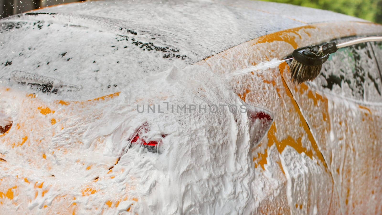 Yellow car completely covered with shampoo and foam, more spraying, in self serve carwash.