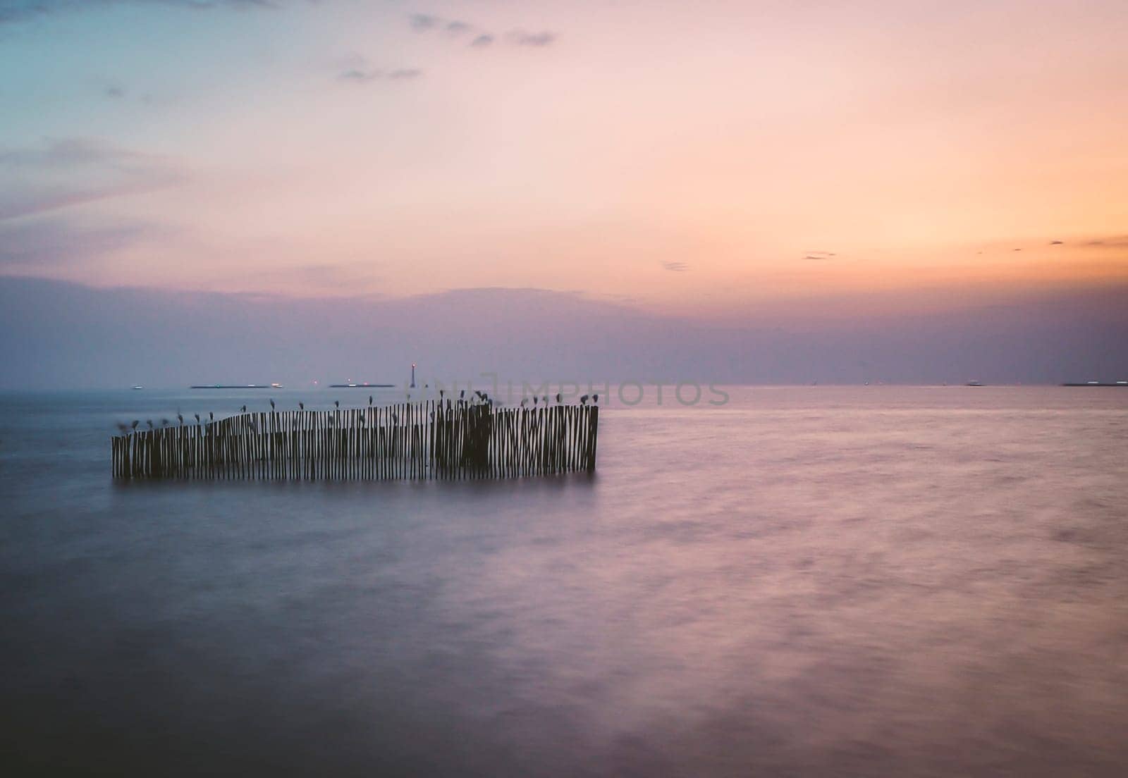 long exposure wooden pole in sea at dusk. Pastel blue and pink sky in Bangpu Thailand