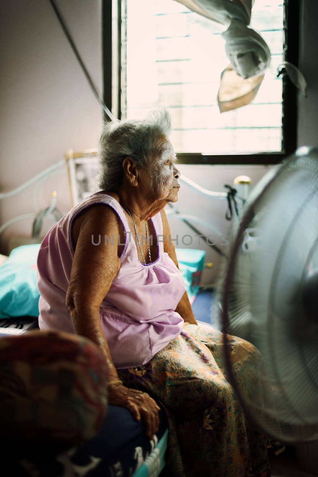 Asian retired woman is sitting in her room and watching news on TV at home. Old woman self isolating during coronavirus outbreak lockdown in Thailand. Quarantine concept.