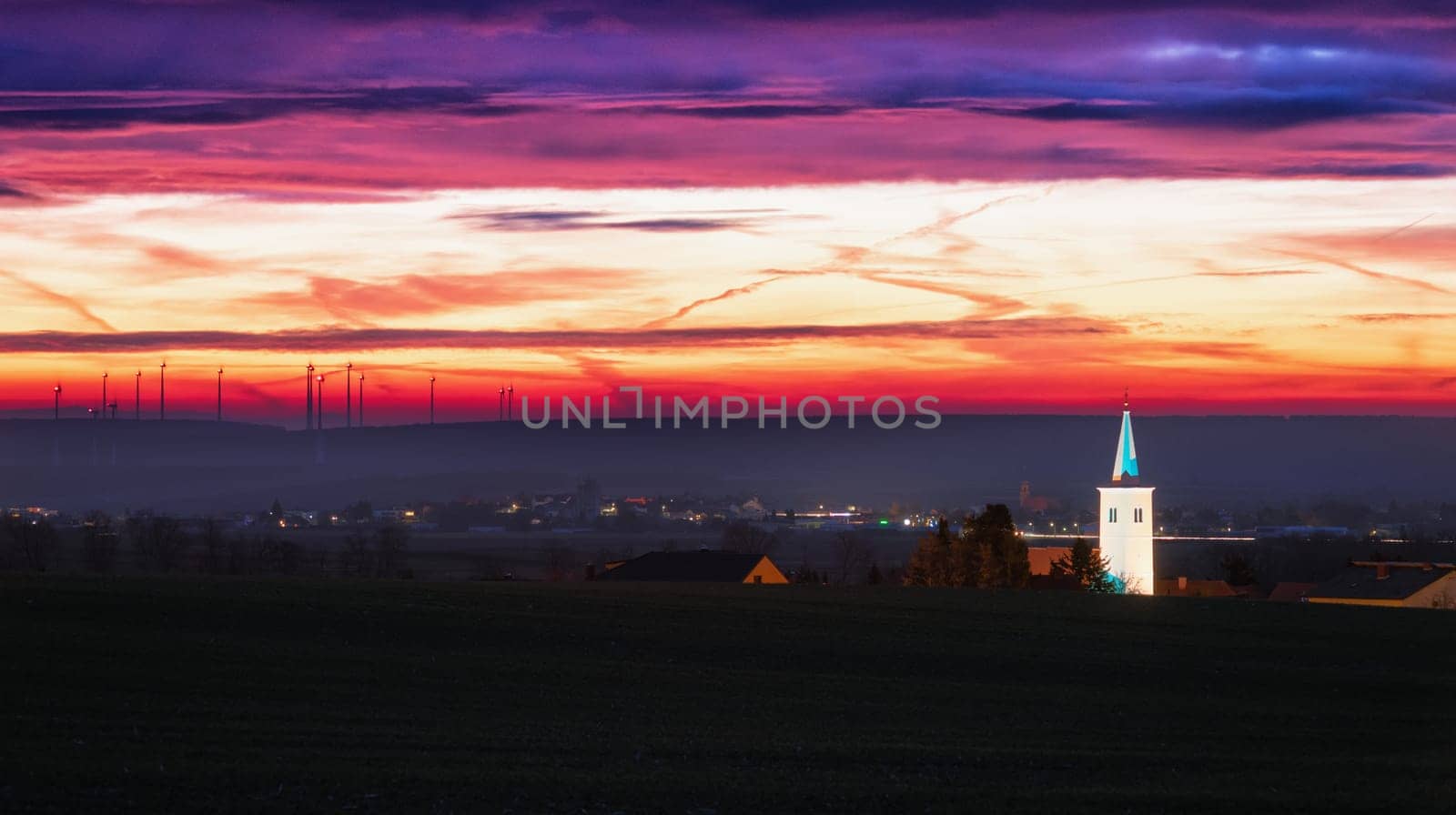 belltower at sunrise illuminated at sunrise with wind turbines