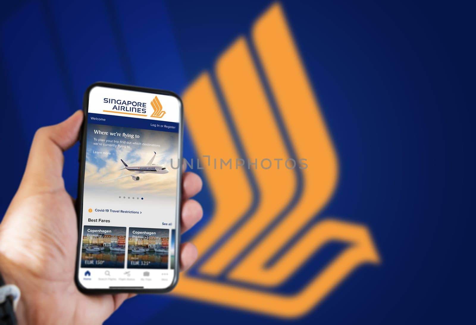 Singapore, October 2021: Hand holding a phone with Singapore Airlines flight booking application. Singapore Airlines logo blurred on a blue background. Booking airline tickets