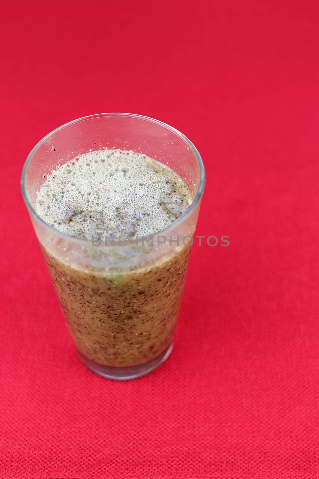 Close-up of blended papaya seeds, pulp and water in a drinking glass close-up on a red place mat. Pureed blend of fresh papaya seeds, papaya pulp and water in a drinking glass on a red background.