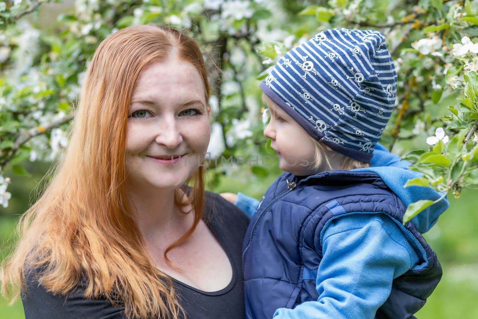 Portrait of young  mother and her cute little son she is holding in her arms under a flowering tree.