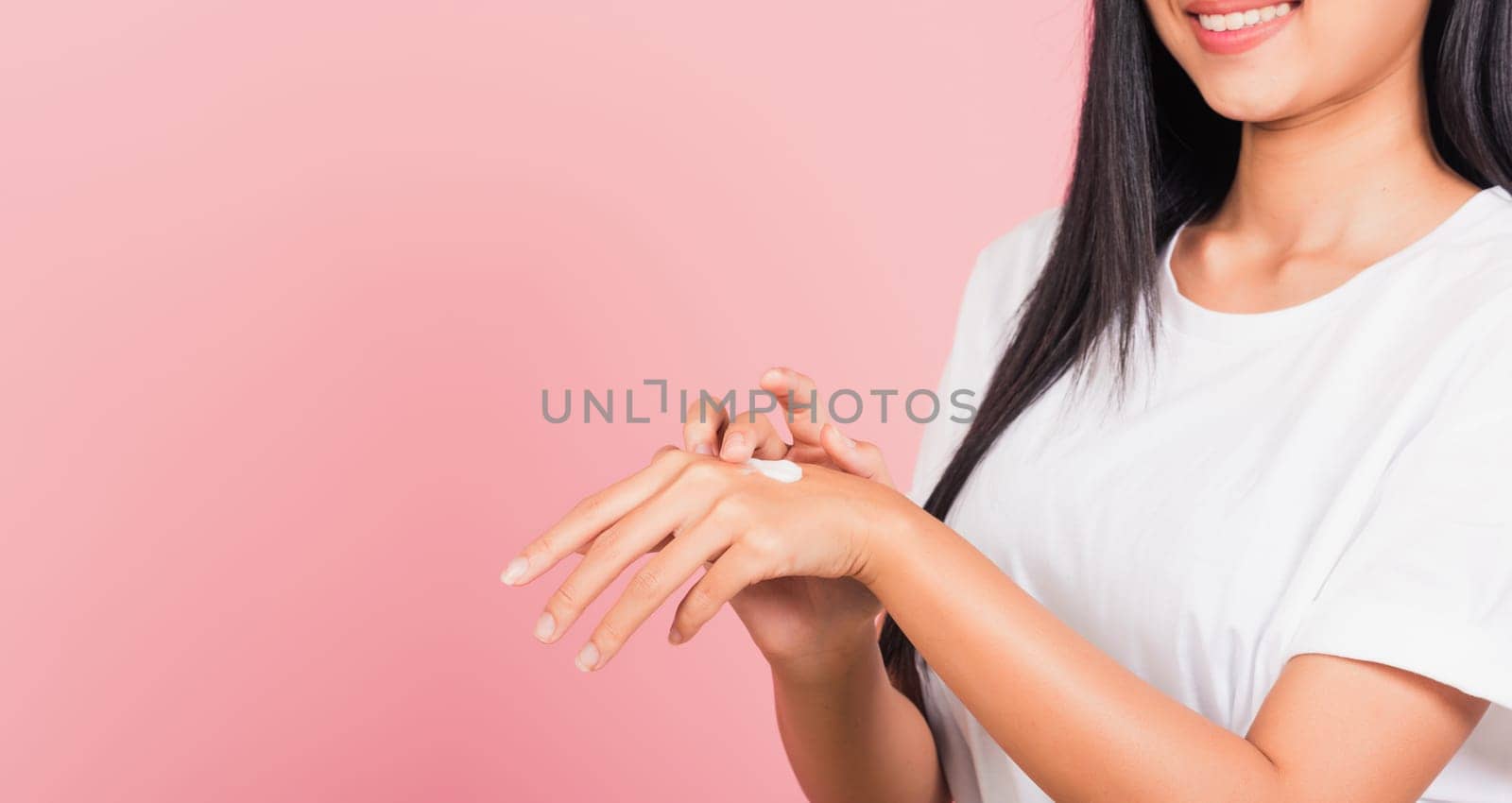 Portrait of Asian beautiful young woman applying lotion cosmetic moisturizer cream on her behind the palm skin back hand, studio shot isolated on pink background,  Hygiene skin body care concept