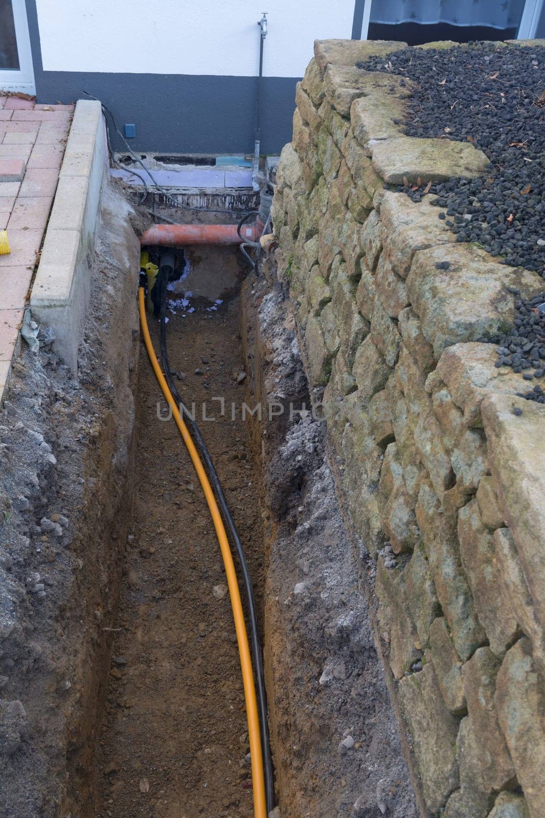 Work on the installation of engineering and heating systems. Two plastic pipes one yellow for gas pipe and one black for power lines. They are in a sand ditch.