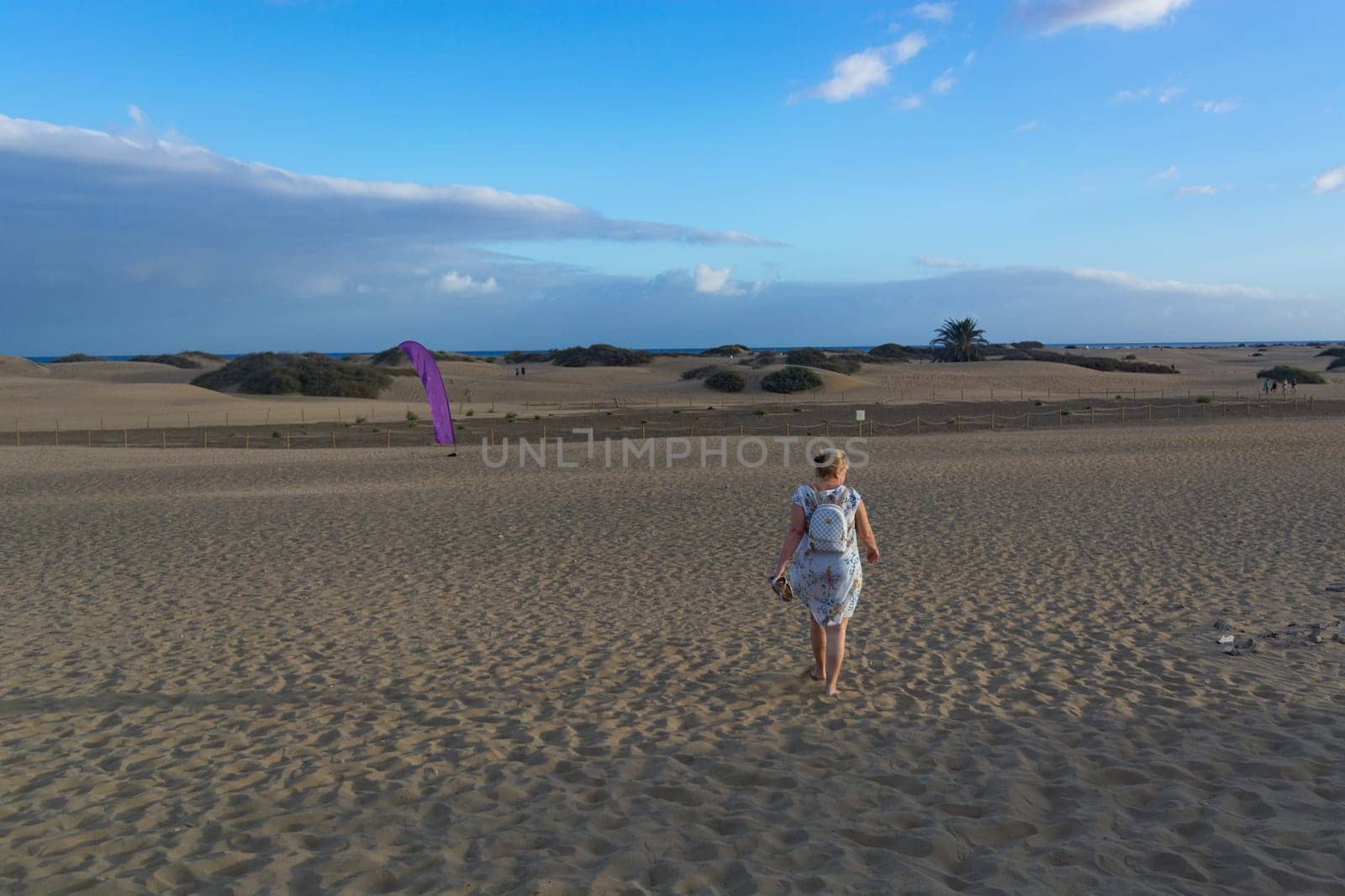 Woman in dress walking in the sand of desert dunes with steps in the desert sand, young woman walking in white sand on a bright summer day, holiday vacation concept