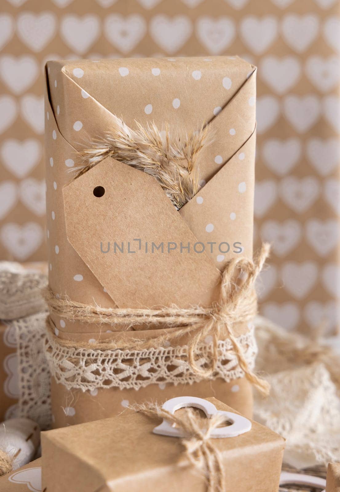 Valentines kraft paper wrapped present with vertical gift tag, hearts and pampas grass close up. Spring scene with blank label. Rustic, cottage chic or bohemian mockup, copy space
