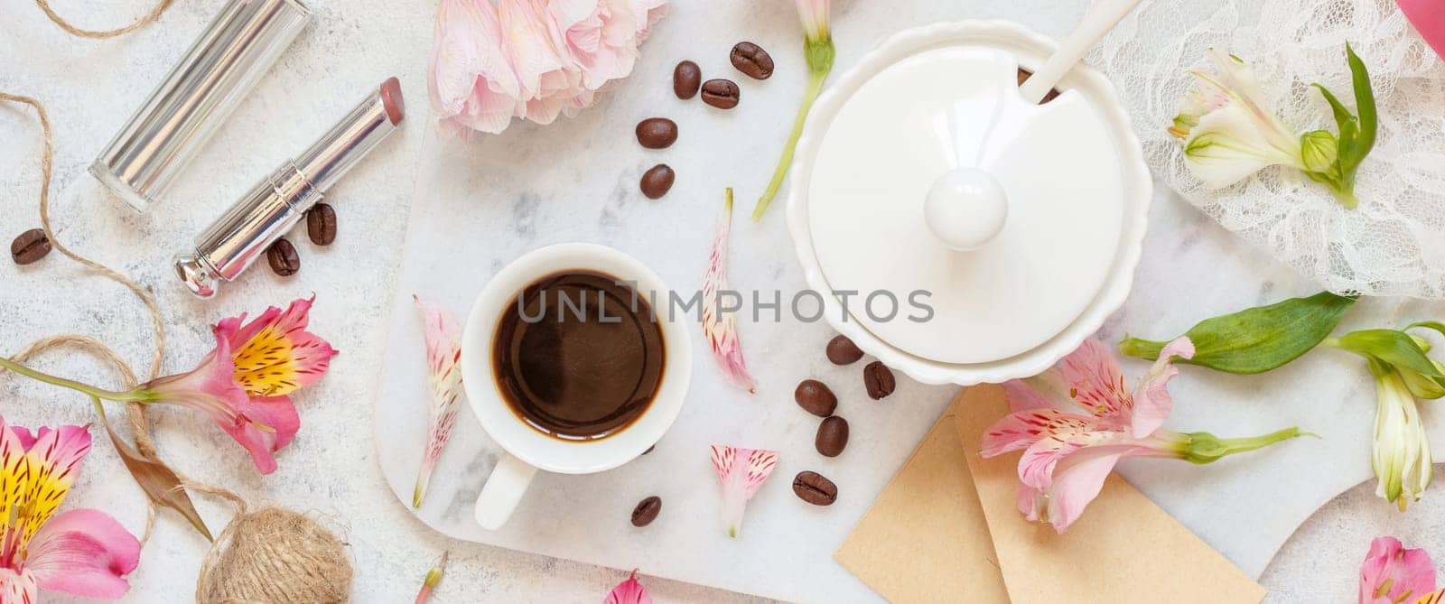 Coffee cup near pink flowers, lipstick and envelope on white table top view. Romantic breakfast
