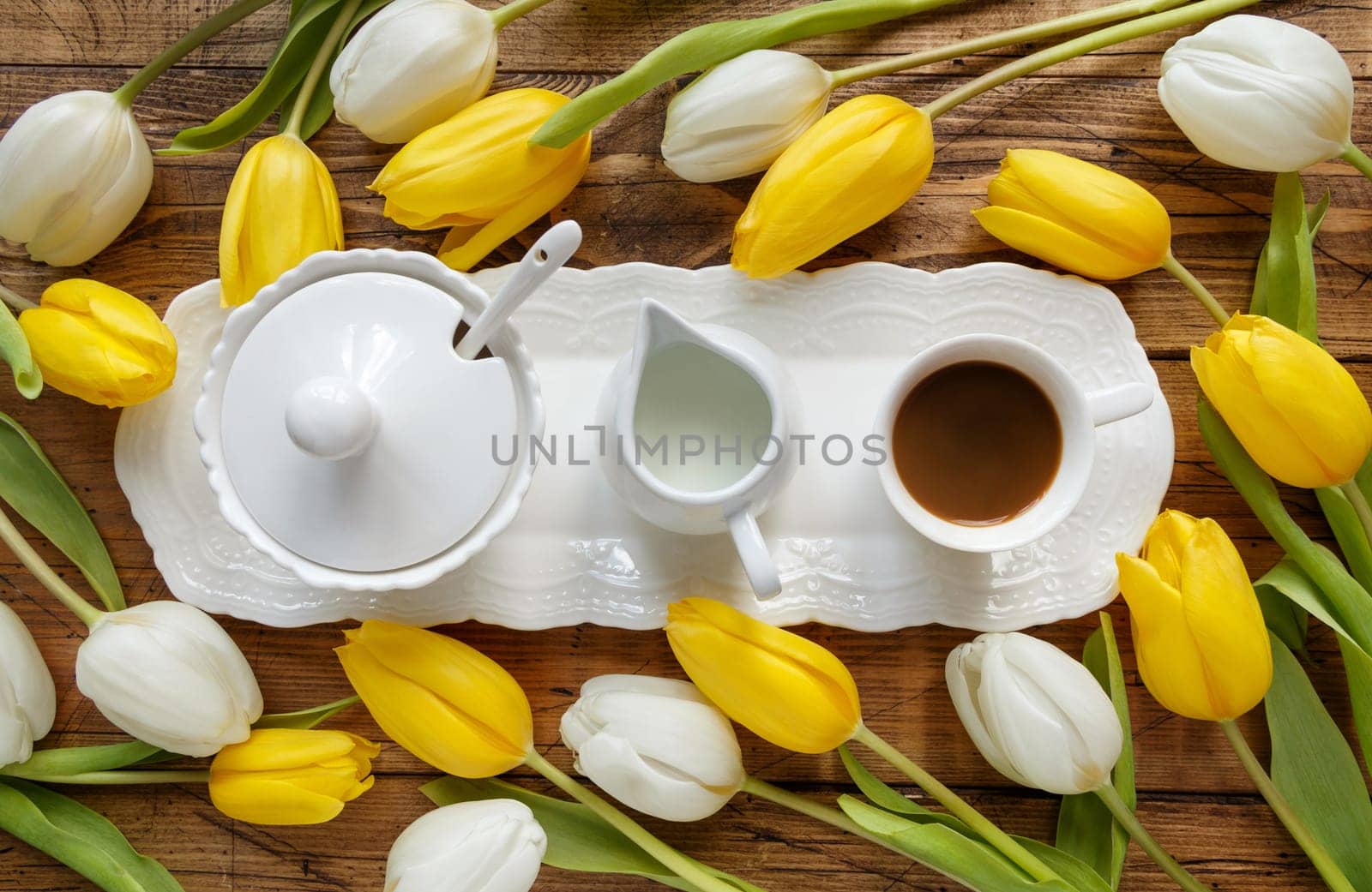 Coffee tray between white and yellow tulips on wooden table top view