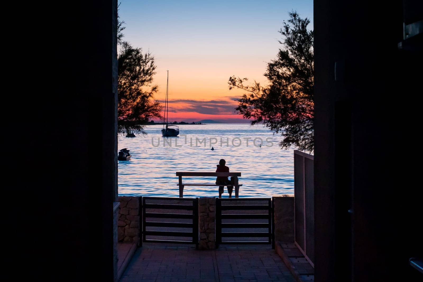 A woman sitting on a bench by the sea at sunset and watching the sea and sunset.
