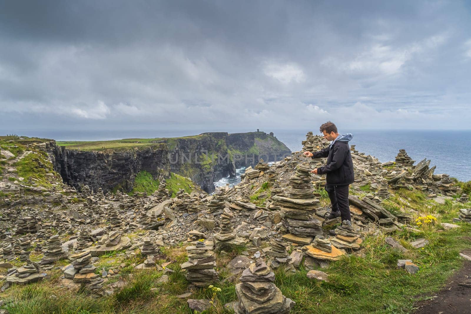 Man, adult stone stacking or rock balancing in iconic Cliffs of Moher, popular tourist attraction, Wild Atlantic Way, County Clare, Ireland